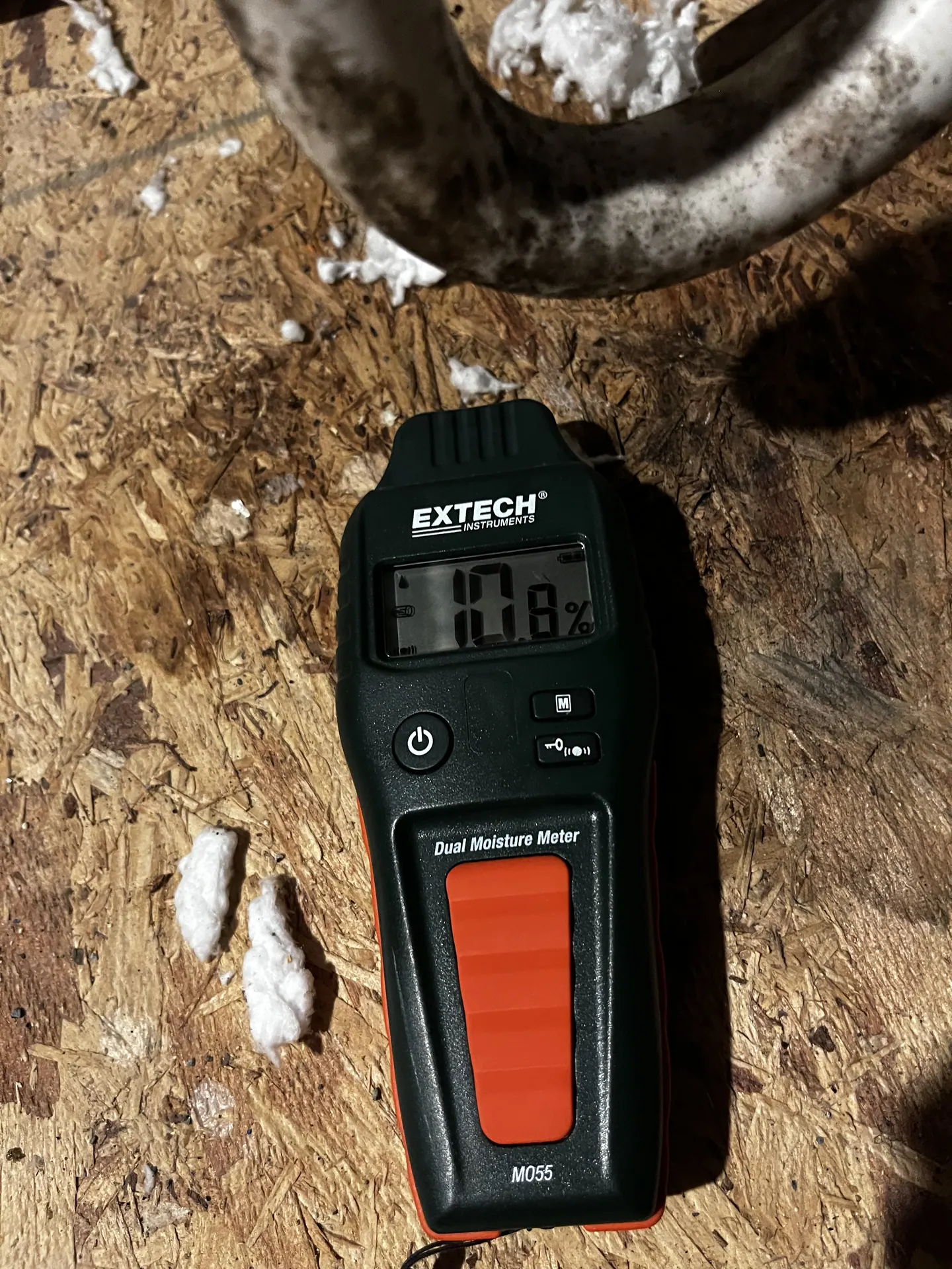 Comparative moisture-meter display reading 10.8 at stained attic decking beneath condensate piping