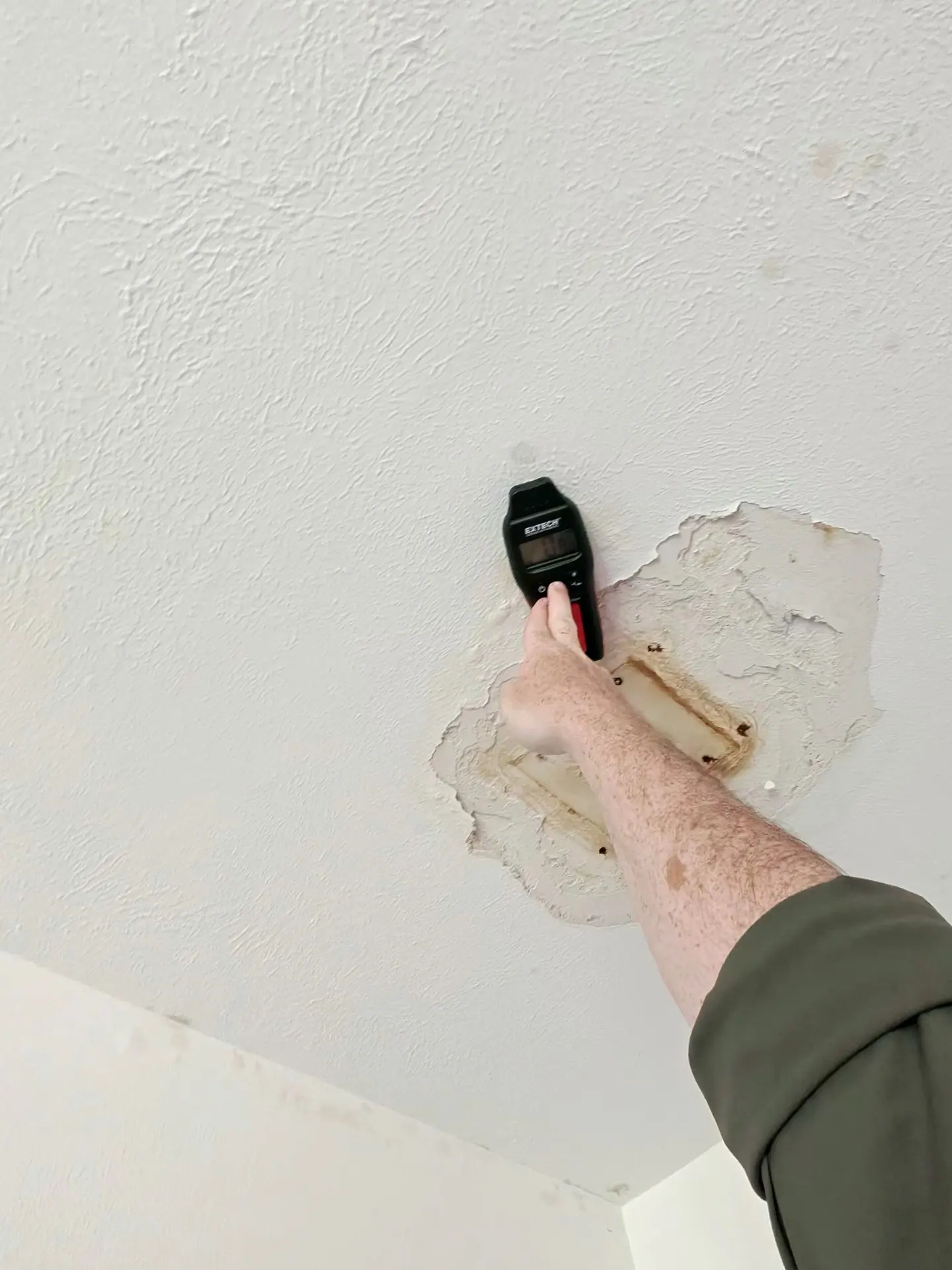 Historic ceiling leak stain with peeled paint and a comparative moisture-meter reading