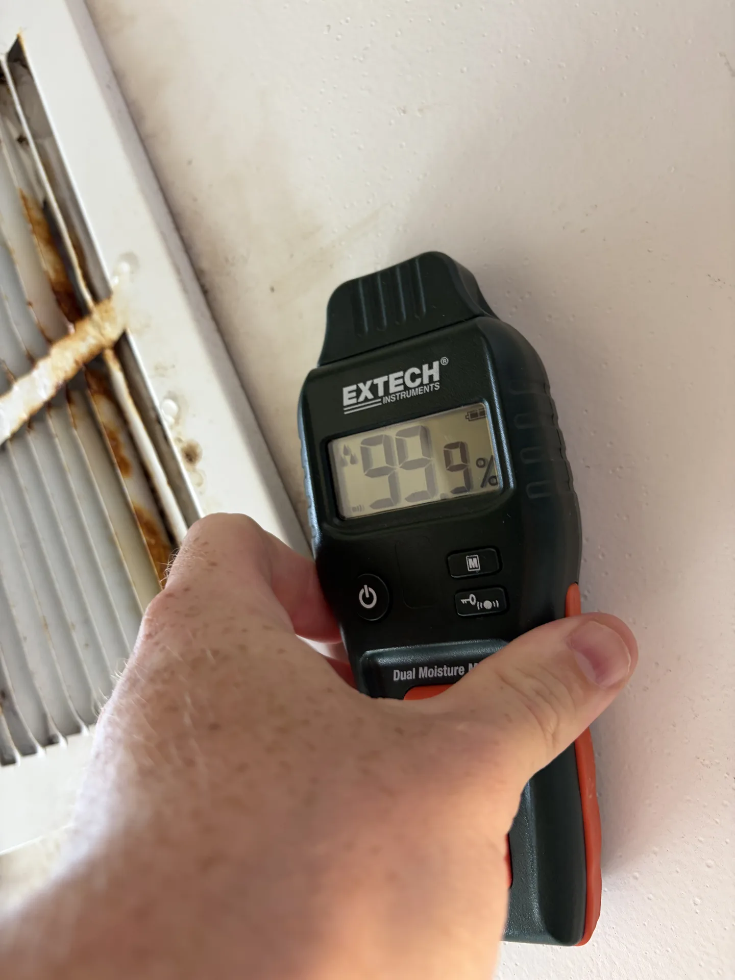 Comparative pinless moisture reading of 99.9 beside a wet HVAC supply register