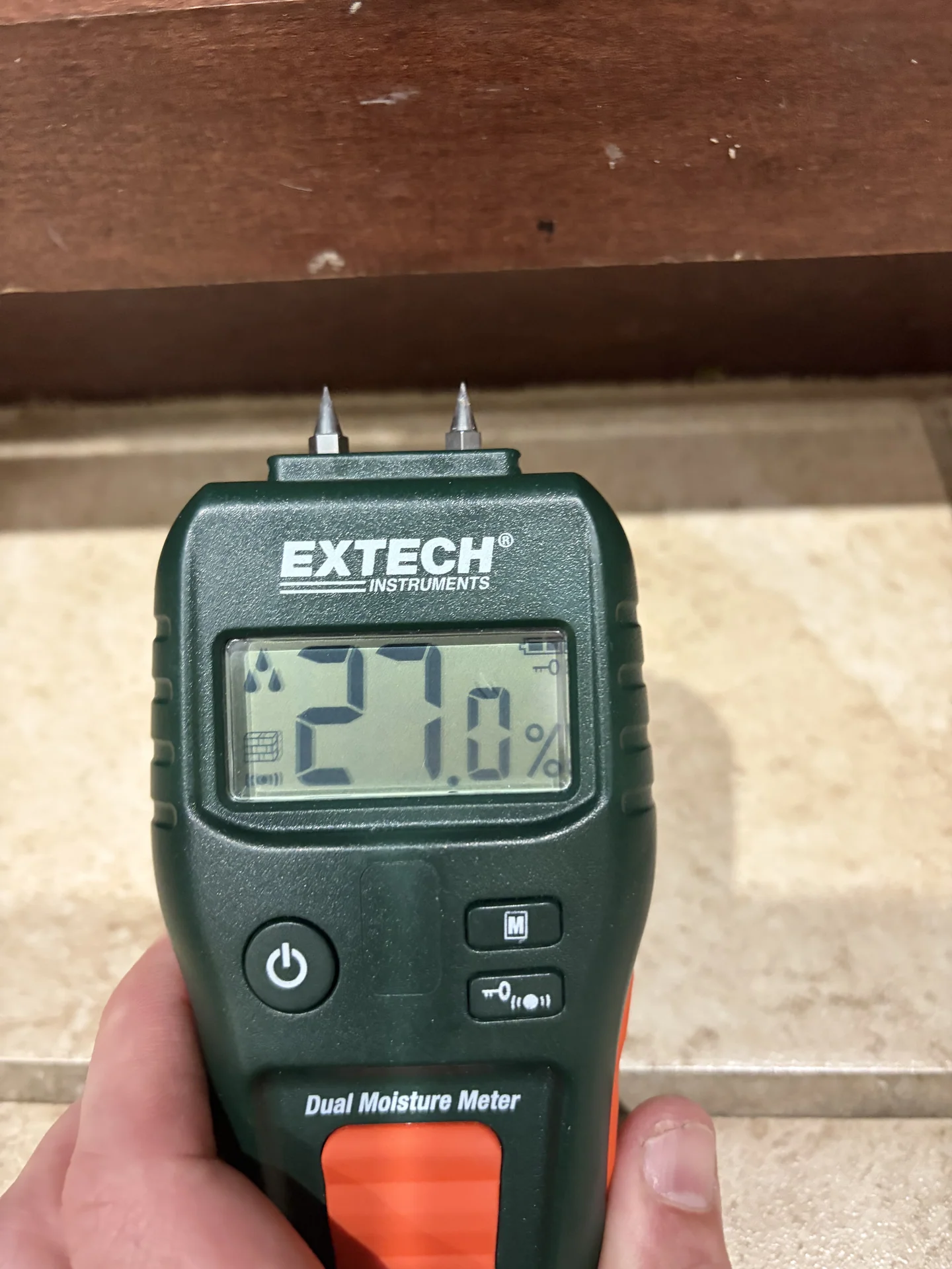 Wood-scale pin moisture reading of 27.0 percent on kitchen cabinet toe kick