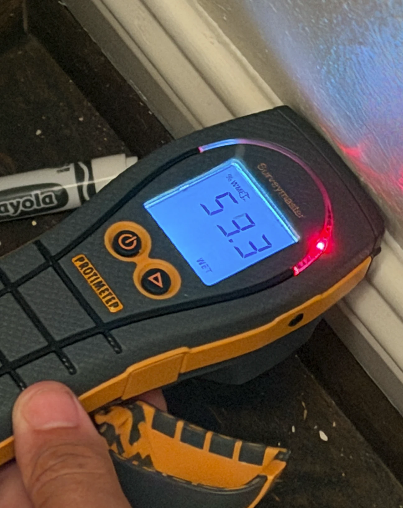 Contractor's Protimeter display reading 59.3 on the %WME scale with WET indication at the office-closet shared wall